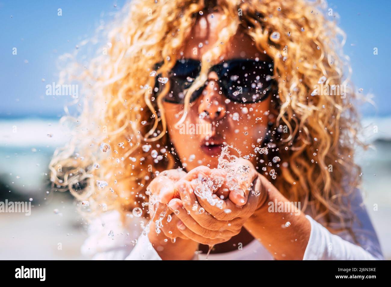 Nahaufnahme einer Frau, die Meerwasser aus den Händen bläst und Tropfen tut - Sommermenschen Urlaub und Reise-Lifestyle-Konzept - lockig blonde Frau in Stockfoto