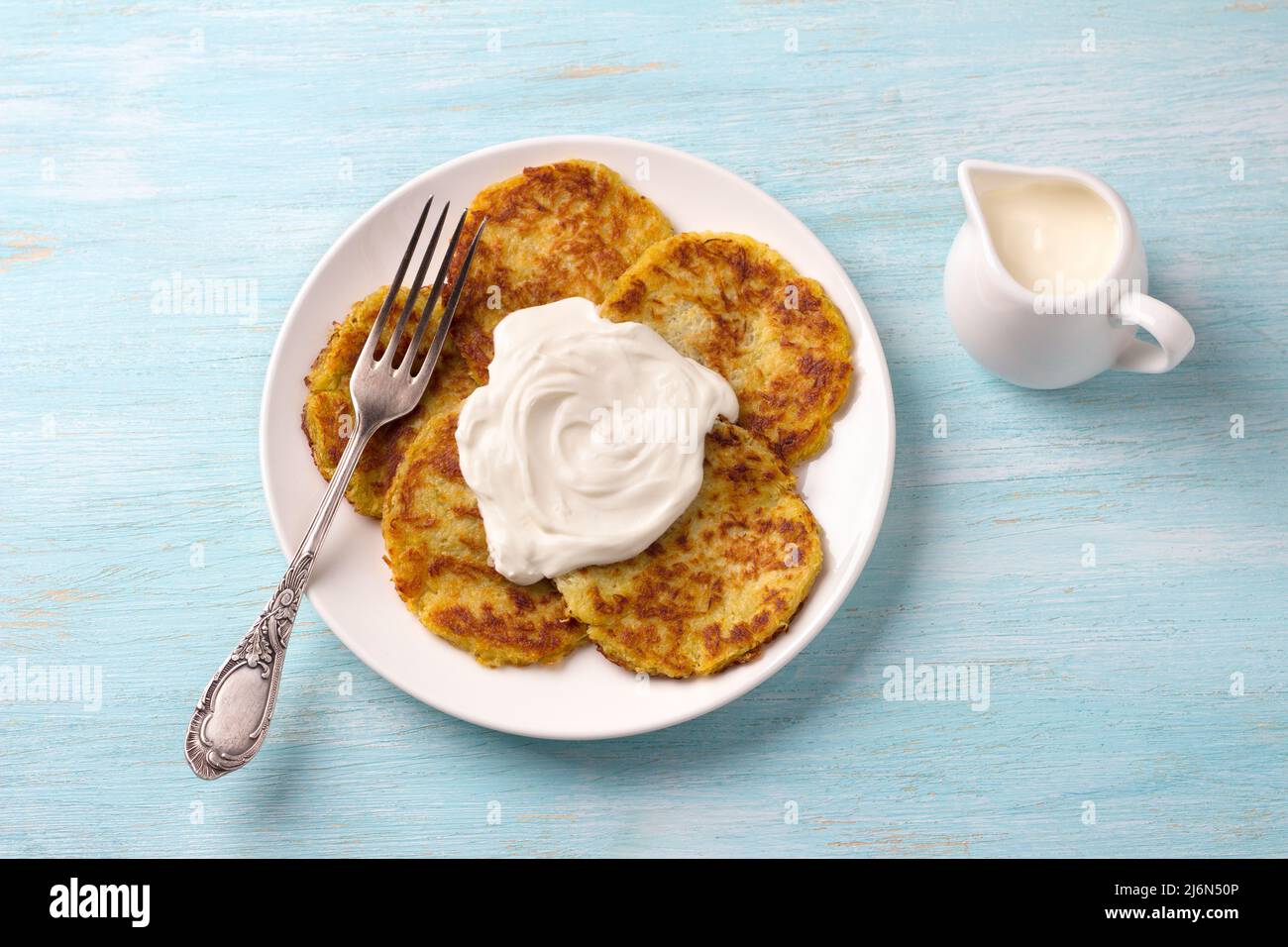 Traditionelle Latkes-Krabben mit saurer Creme auf hellblauem texturiertem Hintergrund, Draufsicht Stockfoto