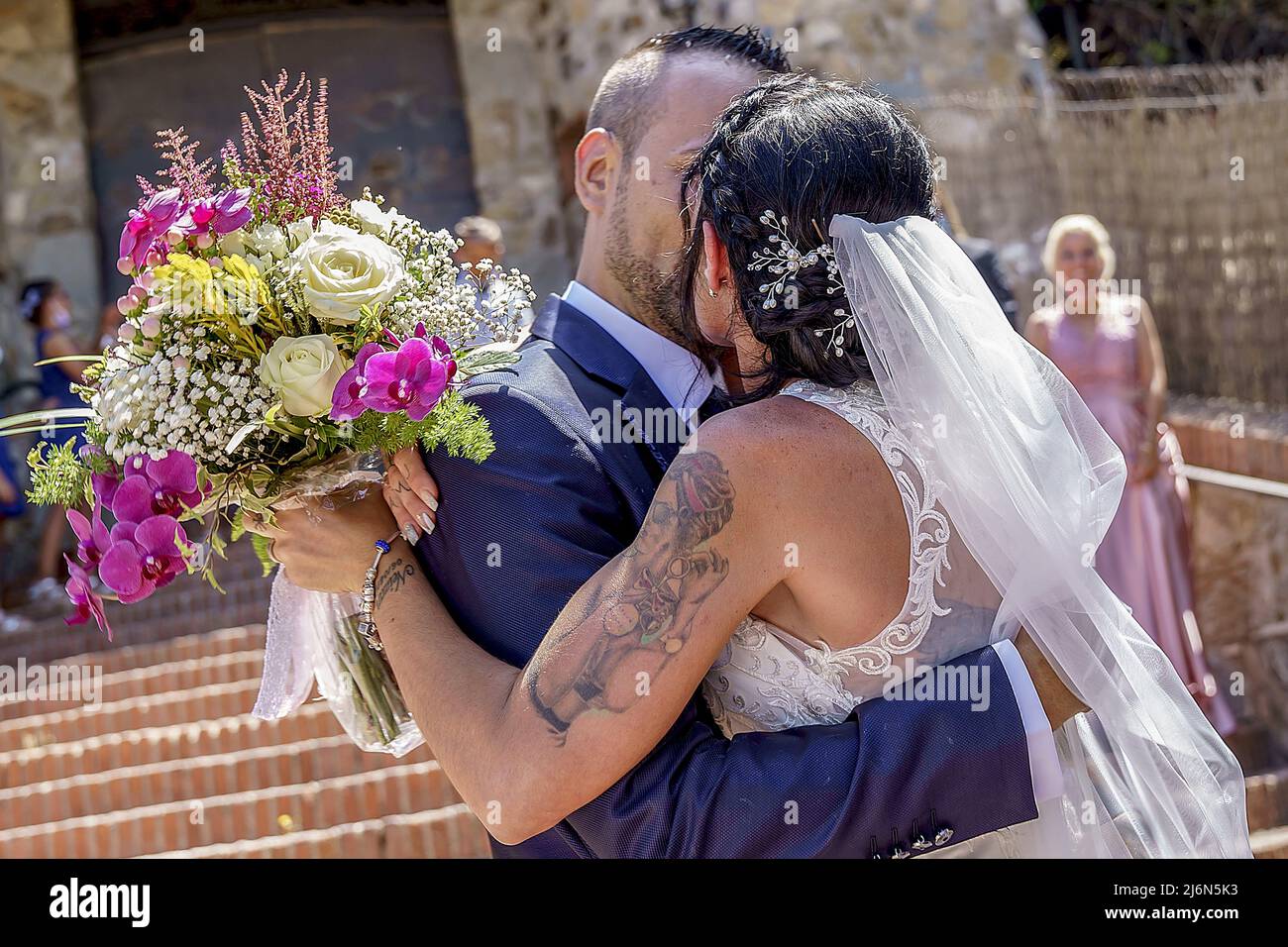 Brautpaar umarmt und küsst sich mit Brautstrauß. Stockfoto