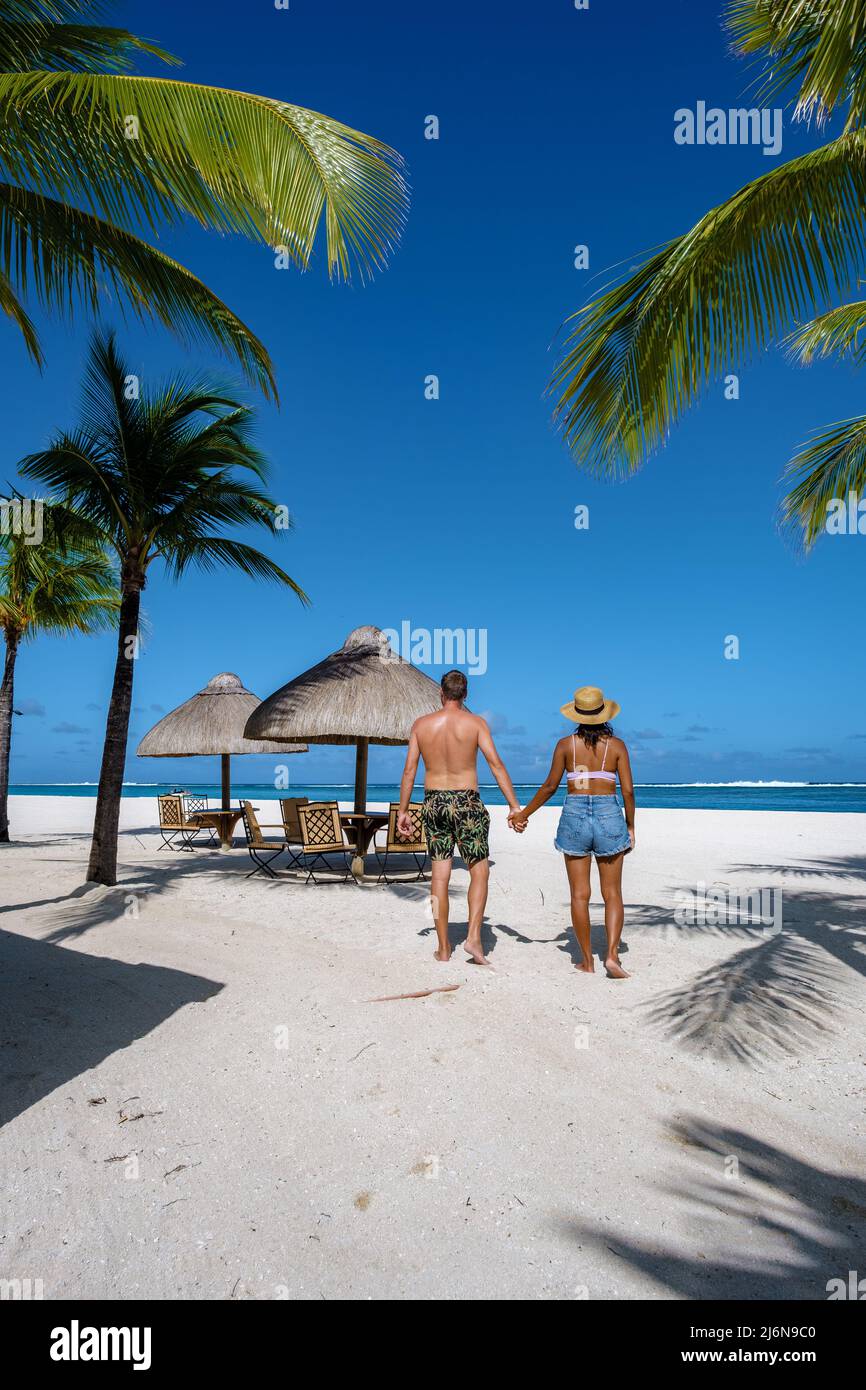 Tropischer Strand Palmen und weißer Sand blaues Meer und Strandliegen Sonnenschirme, Liegestühle und Sonnenschirme unter einer Palme an einem tropischen Strand. Paar Männer und Frauen am tropischen Strand Le Morne Mauritius Stockfoto