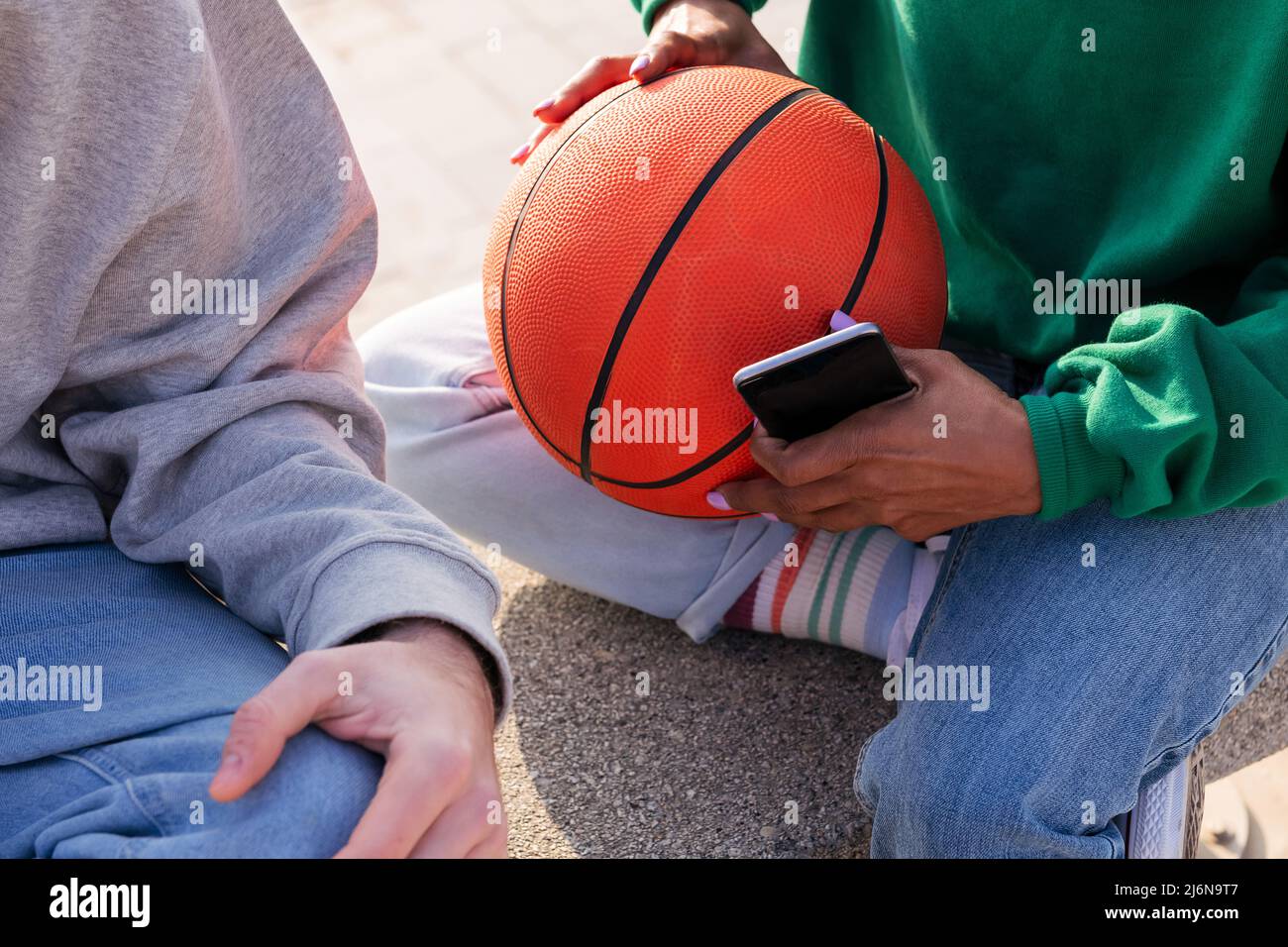 Detail der Hände einer Frau, die einen Basketball und ein Smartphone hält, Konzept des Sports und des modernen Lebensstils Stockfoto