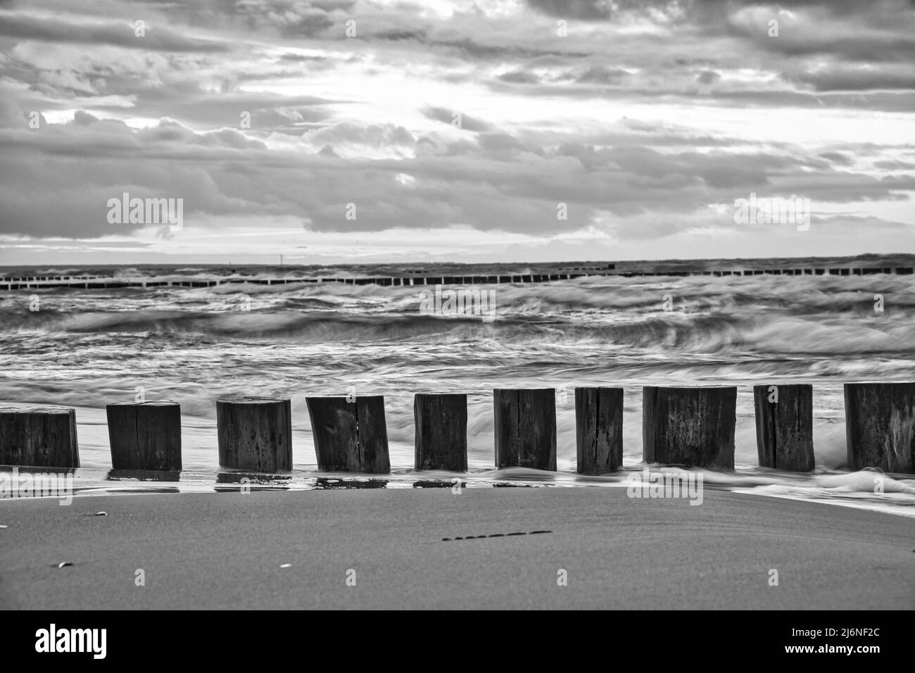 Sonnenuntergang am Ostseestrand in schwarz-weiß. Groynes vor Meer und Himmel. Blaue Stunde mit Wolken am Himmel. Landschaftsfoto in Zi Stockfoto