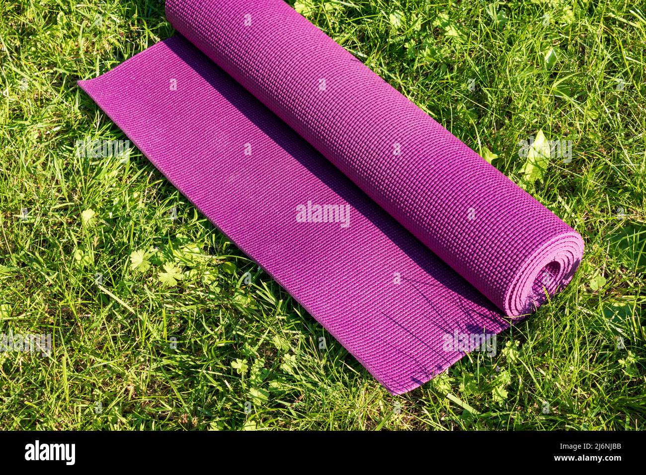 Rolled Yoga Matte auf grünem Gras mit Sonnenlicht, Nahaufnahme direkt darüber. Outdoor-Sportkonzept Stockfoto