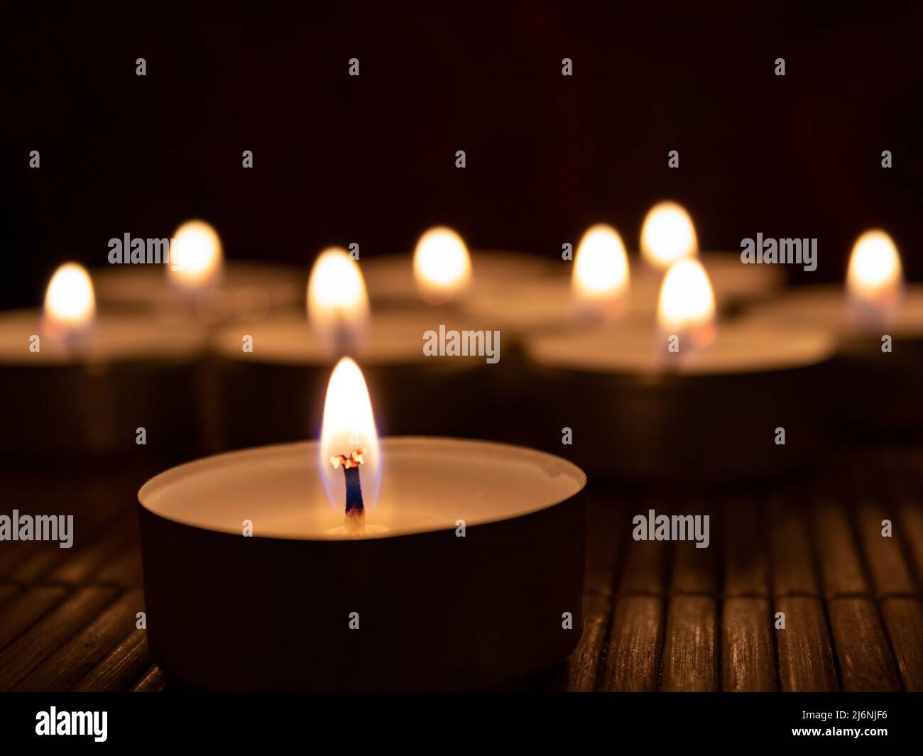 Warmes Kerzenlicht von Teelichtkerzen auf Bambusoberfläche in einer dunklen und entspannten Atmosphäre Stockfoto