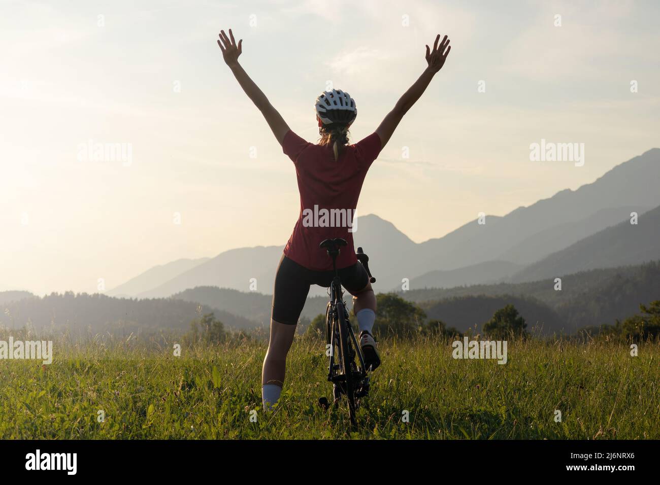 Glückliche Radfahrerin vor Freude, mit über ihrem Kopf erhobenen Armen und Blick auf den Sonnenuntergang Stockfoto