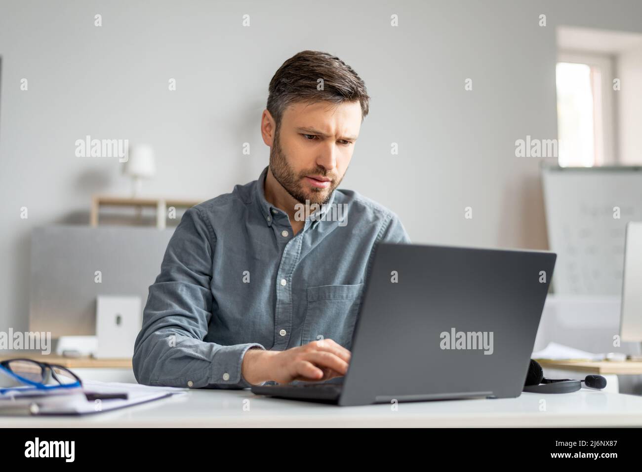 Reifer männlicher Manager, der im modernen Büro am Laptop arbeitet, am Tisch sitzt und auf der Computertastatur tippt Stockfoto