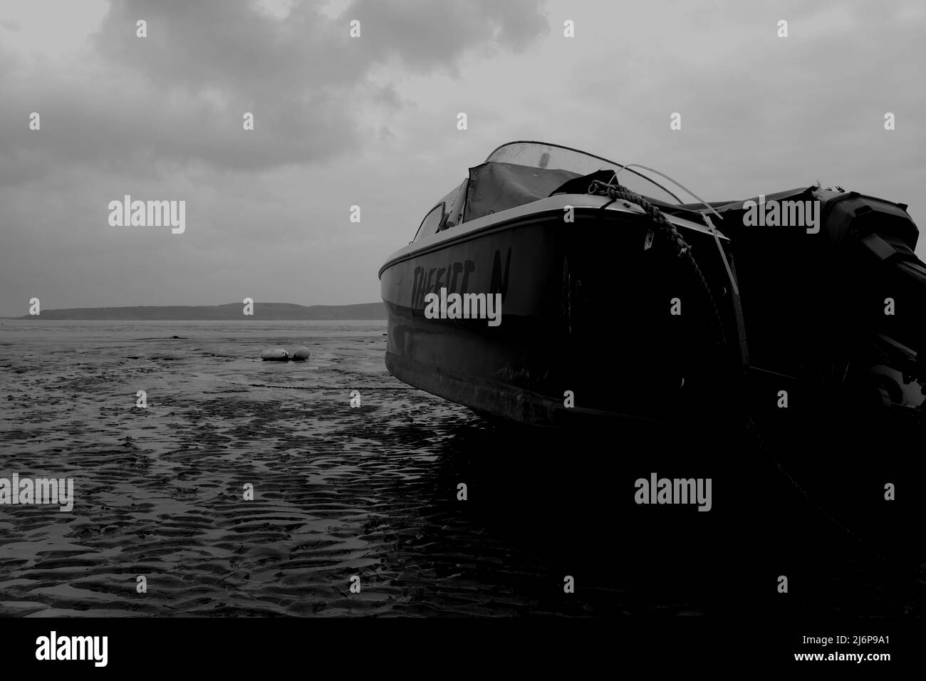 Eine monochrome Aufnahme eines Bootes mit Blick auf das Meer, das im Schlamm an einem Strand festsitzt Stockfoto