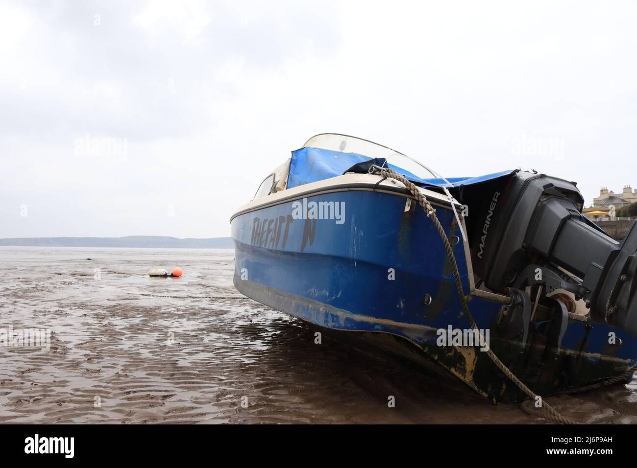 Mit Blick auf das Meer und wenig Hoffnung, bald befreit zu werden - ein blaues Boot steckte an einem schlammigen Strand fest Stockfoto