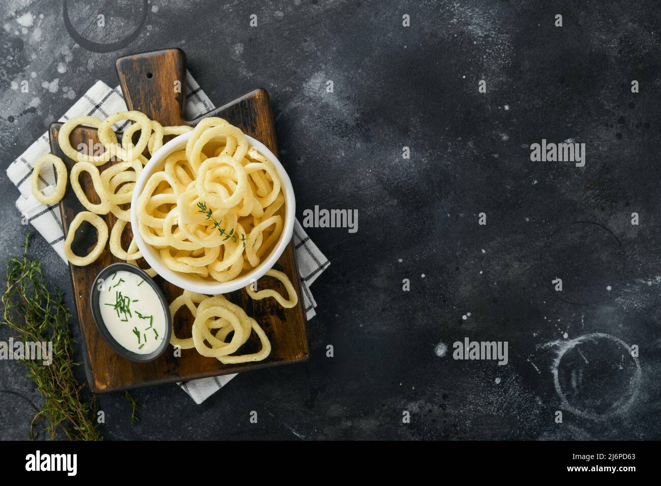 Zwiebelringe. Fast Food. Knusprige Zwiebelchips in schwarzer Keramikschüssel mit saurer Rahmsoße und Zwiebeln in Holzständer auf altem schwarzen Betonhintergrund. Am Stockfoto