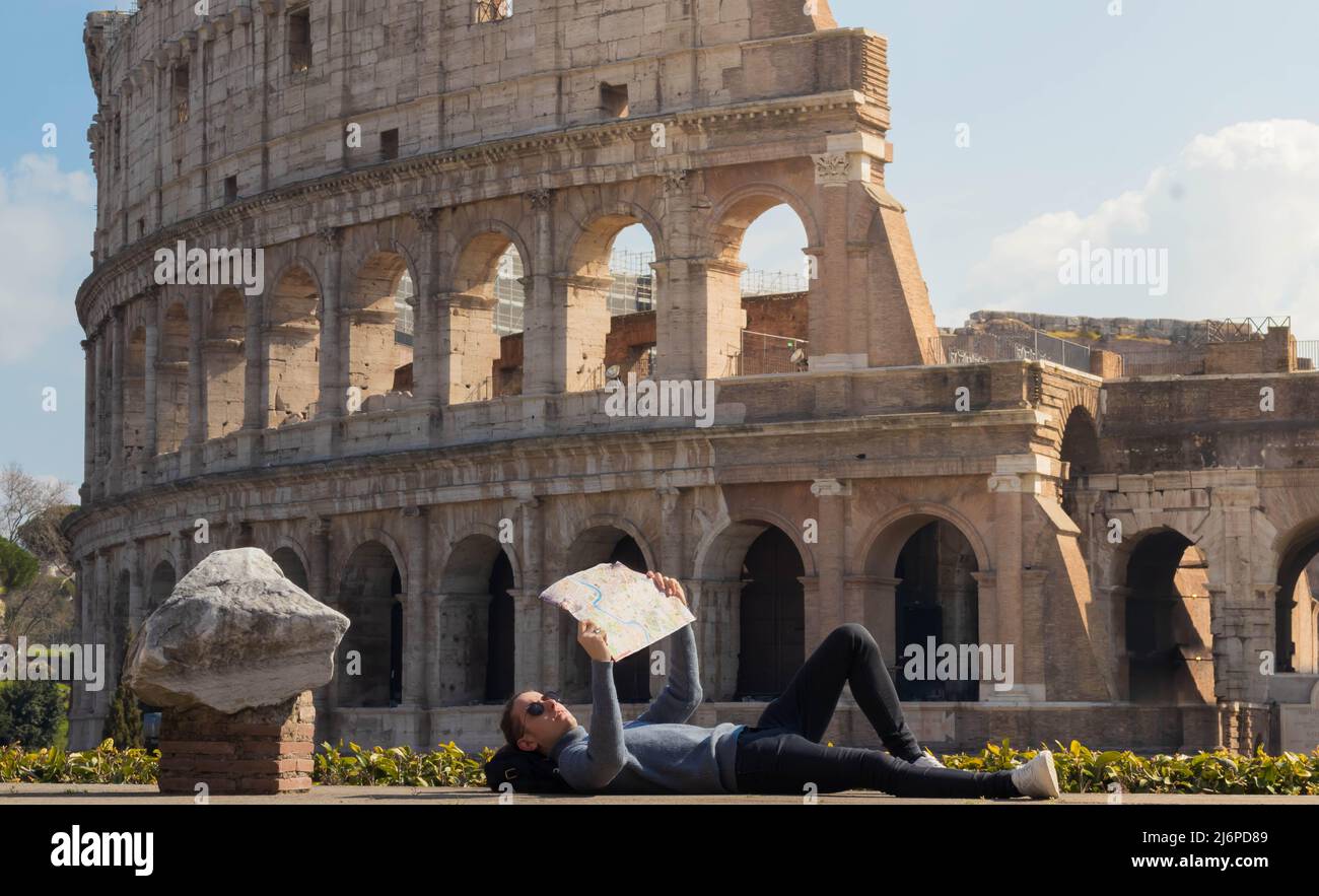 Junger Mann, der sich in der europäischen Stadt Rom in Italien ausruhte, während er sich eine Karte mit dem römischen Kolosseum im Hintergrund ansah Stockfoto