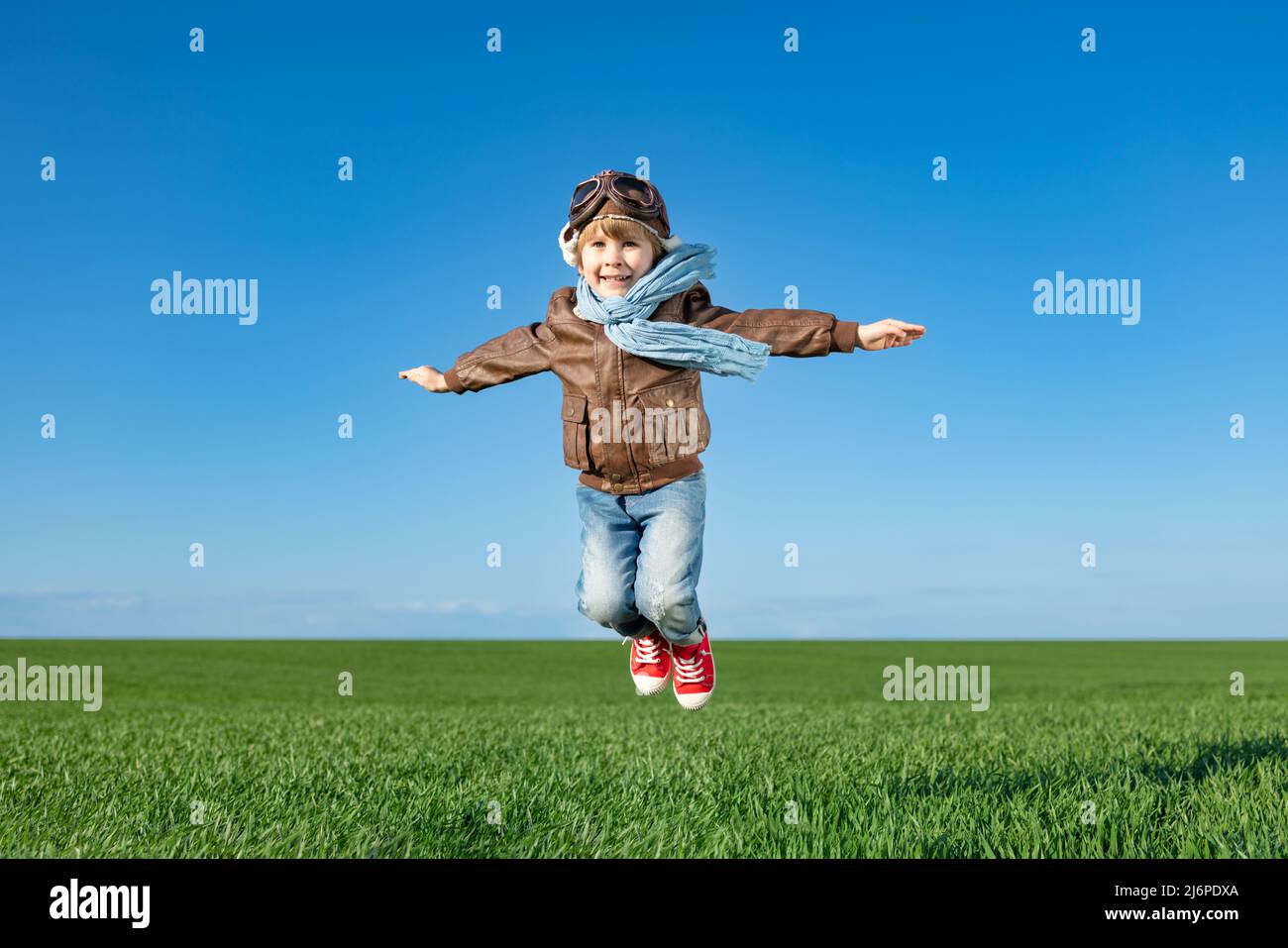 Glückliches Kind springen im Freien in Frühlingsgrün Feld. Kind hat Spaß vor blauem Himmel Hintergrund. Vorstellung und Freiheit Konzept Stockfoto