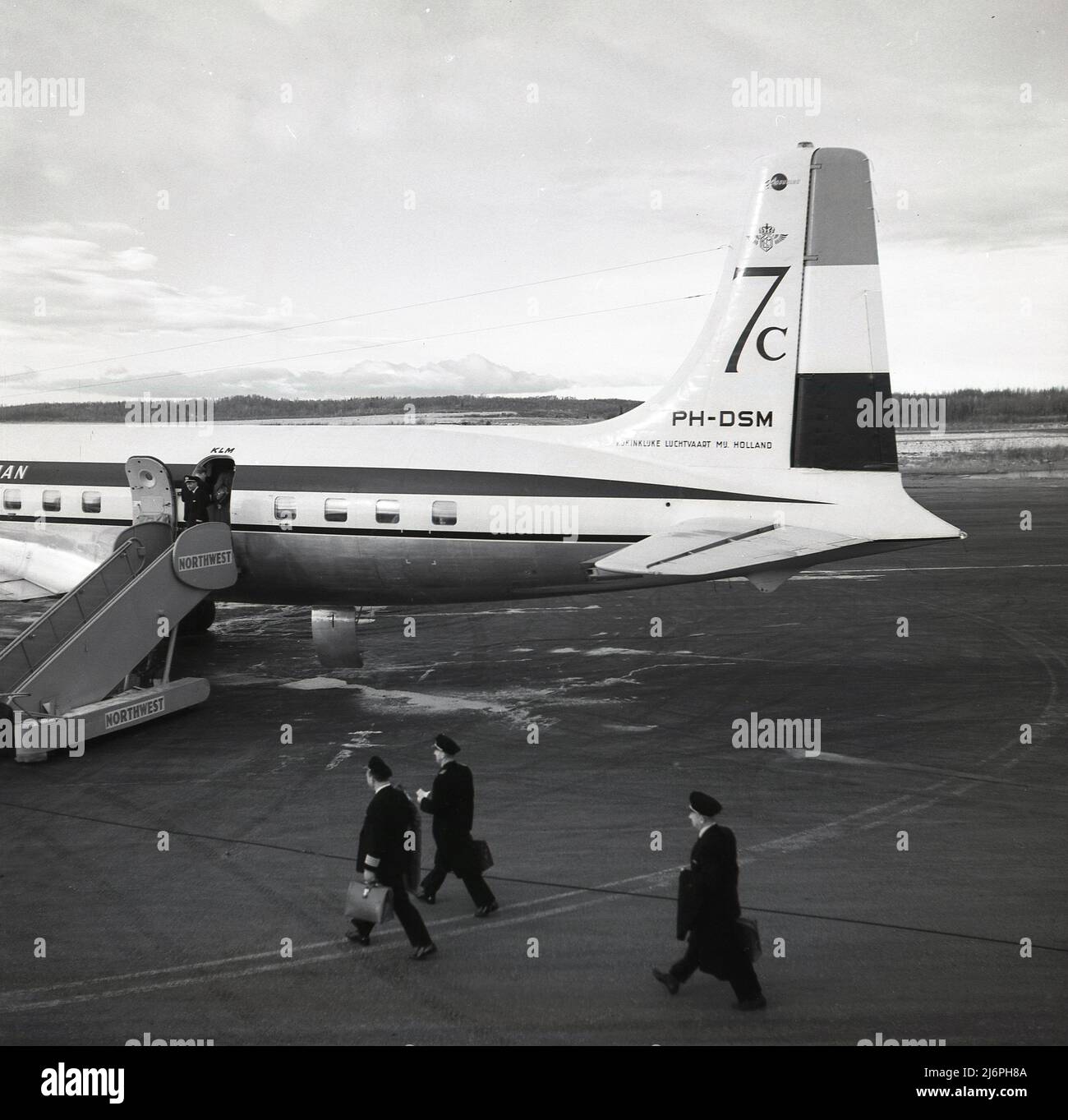 1950s, historisch, Piloten auf der Landebahn zu Fuß an Bord einer Douglas DC-7C. KLM-Flugzeug am Flughafen Anchorage, Alaska, USA. Die 1956 eingeführte DC-7C (Seven Seas) war eine erweiterte Variante des ursprünglichen DC-7-Flugzeugs mit verbesserten Motoren und zusätzlicher Kraftstoffkapazität. Diese Änderungen bedeuteten, dass es über eine ununterbrochende transatlantische Kapazität verfügte und zusätzlich europäische Fluggesellschaften anziehen sollte. Die Zahlen 7c können auf dem Reitflugzeug zu sehen. Stockfoto