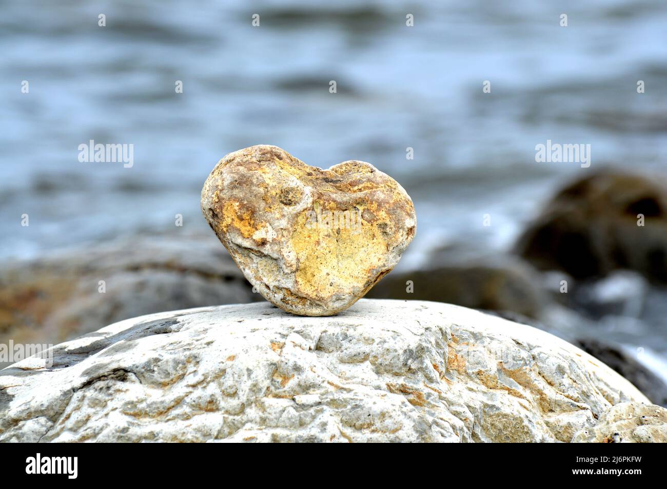 Herzförmiger Stein vor dem Hintergrund des Strandes. Sommersonntag. Liebe, Hochzeit und Valentinstag Konzept. Schöne und interessante Steine finden Stockfoto