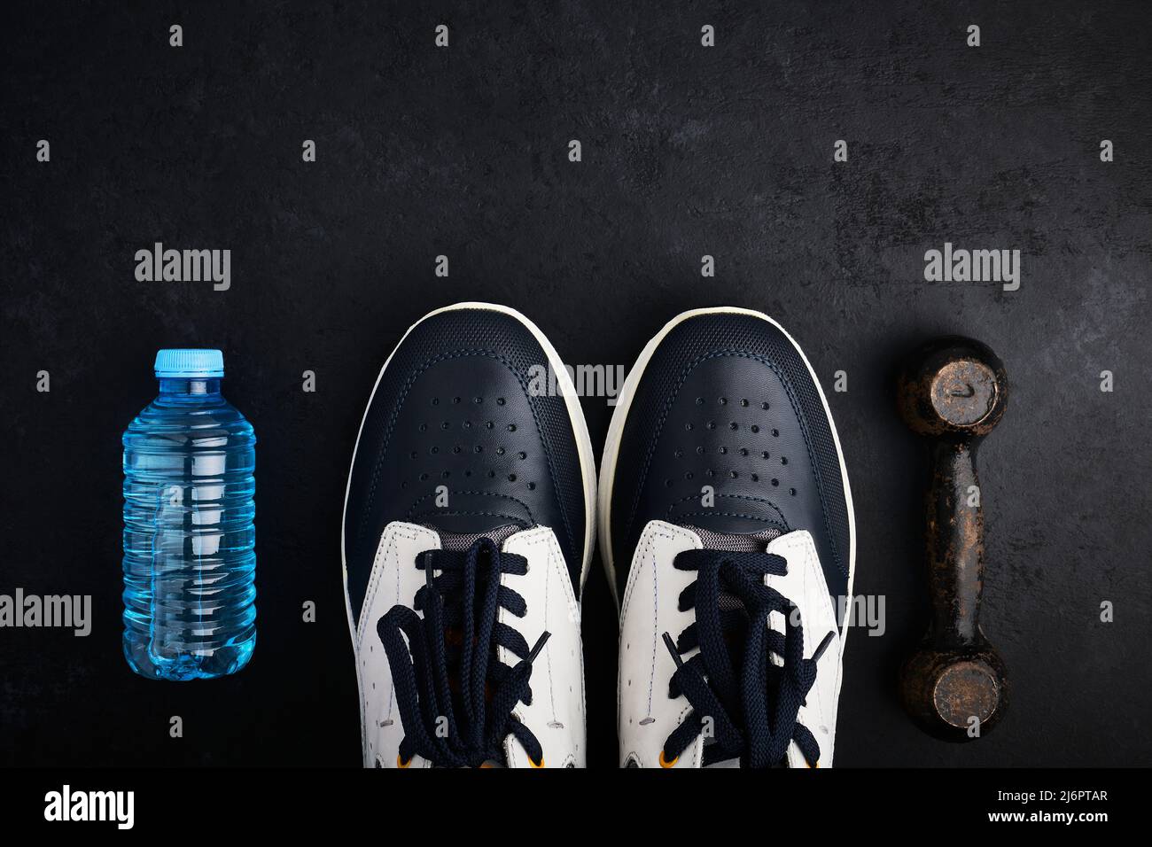 Konzept gesunder Lebensstil, Sportschuhe, Flasche Wasser und alte Hantel auf dunklem Hintergrund mit Kopierfläche Stockfoto