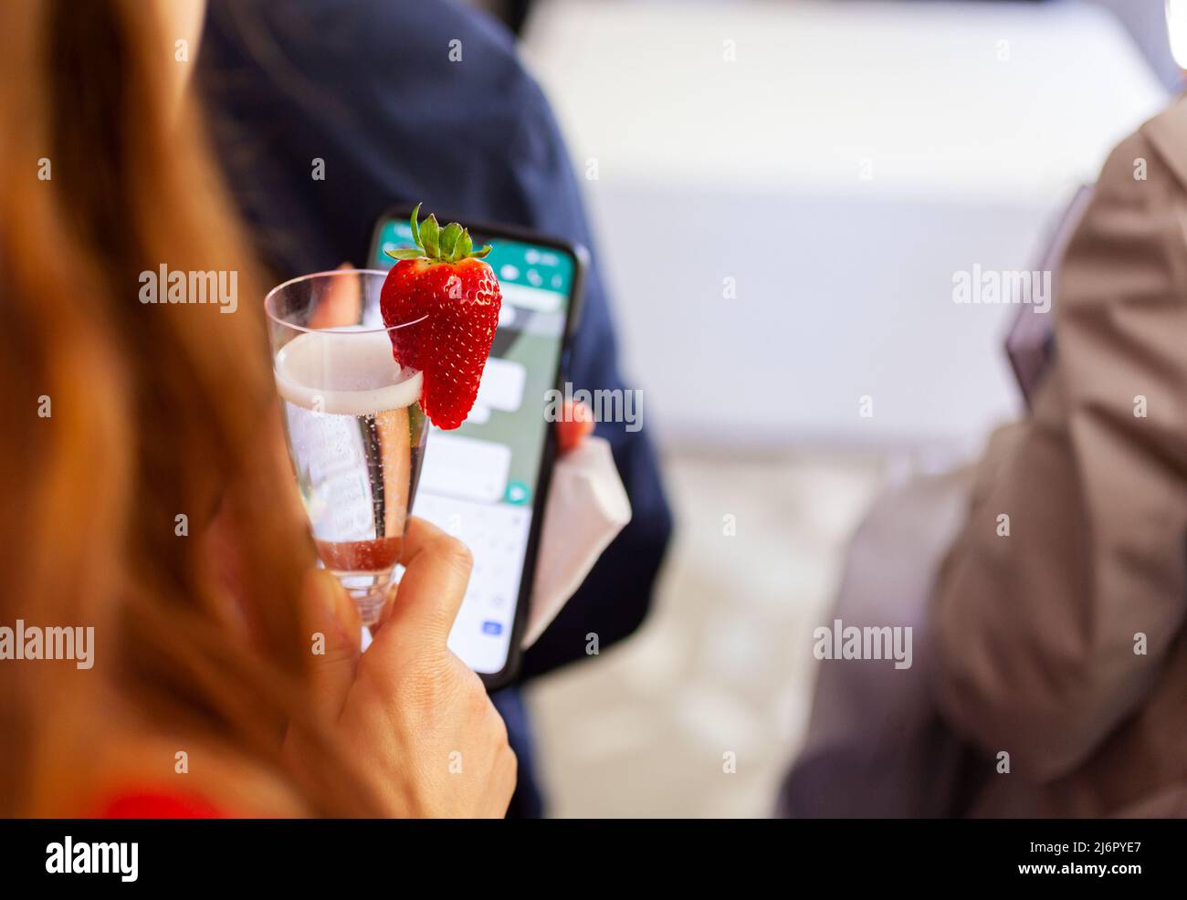 Trinken Sie einen Prosecco-Weißwein mit Erdbeerdekor, während Sie ein Smartphone verwenden Stockfoto