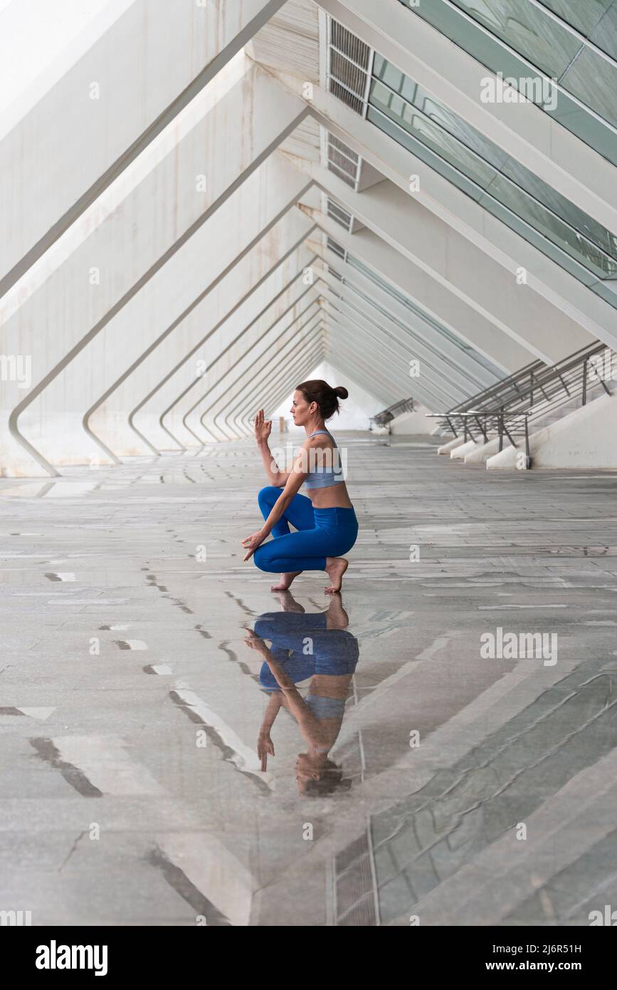 Frau praktiziert Yoga Asana Toe Balance Pose im Freien vor dem Hintergrund der modernen urbanen Architektur. Stockfoto