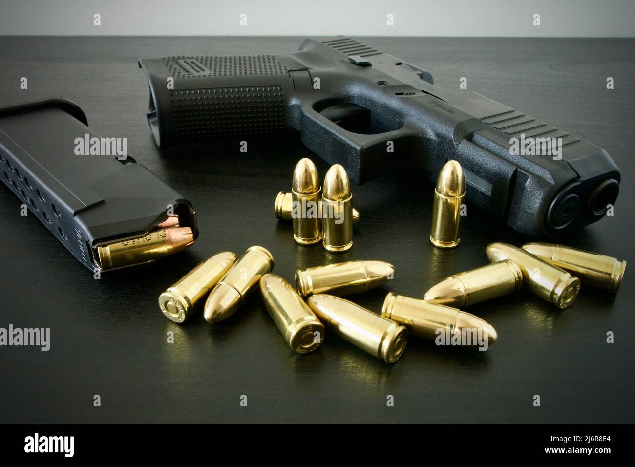 9-mm-Pistole mit voll beladenem Magazin und einem Haufen goldener Messingmunition, die auf einem schwarzen Holztisch verschüttet wurde Stockfoto