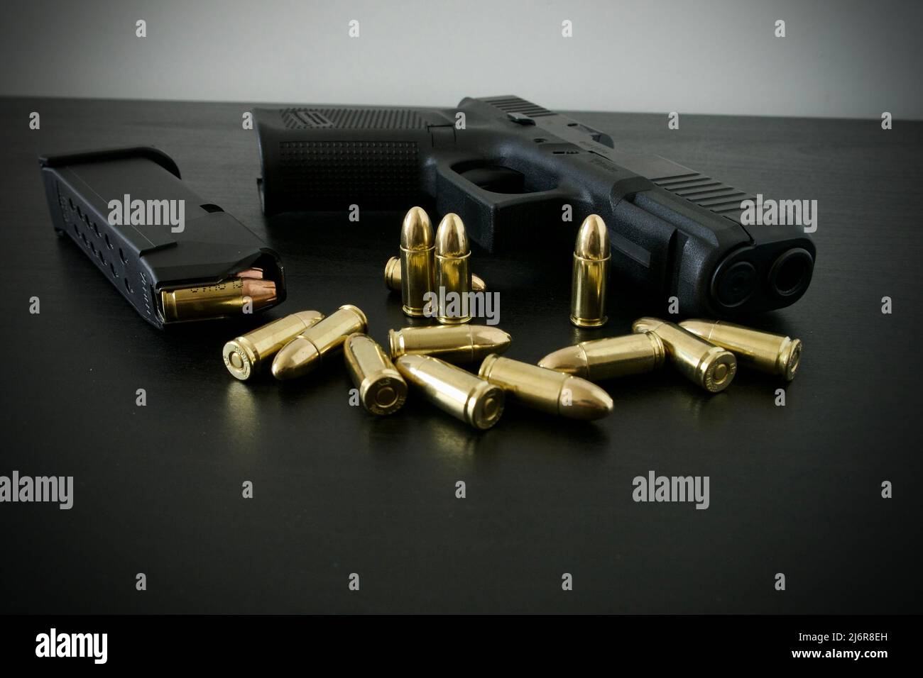 9-mm-Pistole mit voll beladenem Magazin und einem Haufen goldener Messingmunition, die auf einem schwarzen Holztisch verschüttet wurde Stockfoto