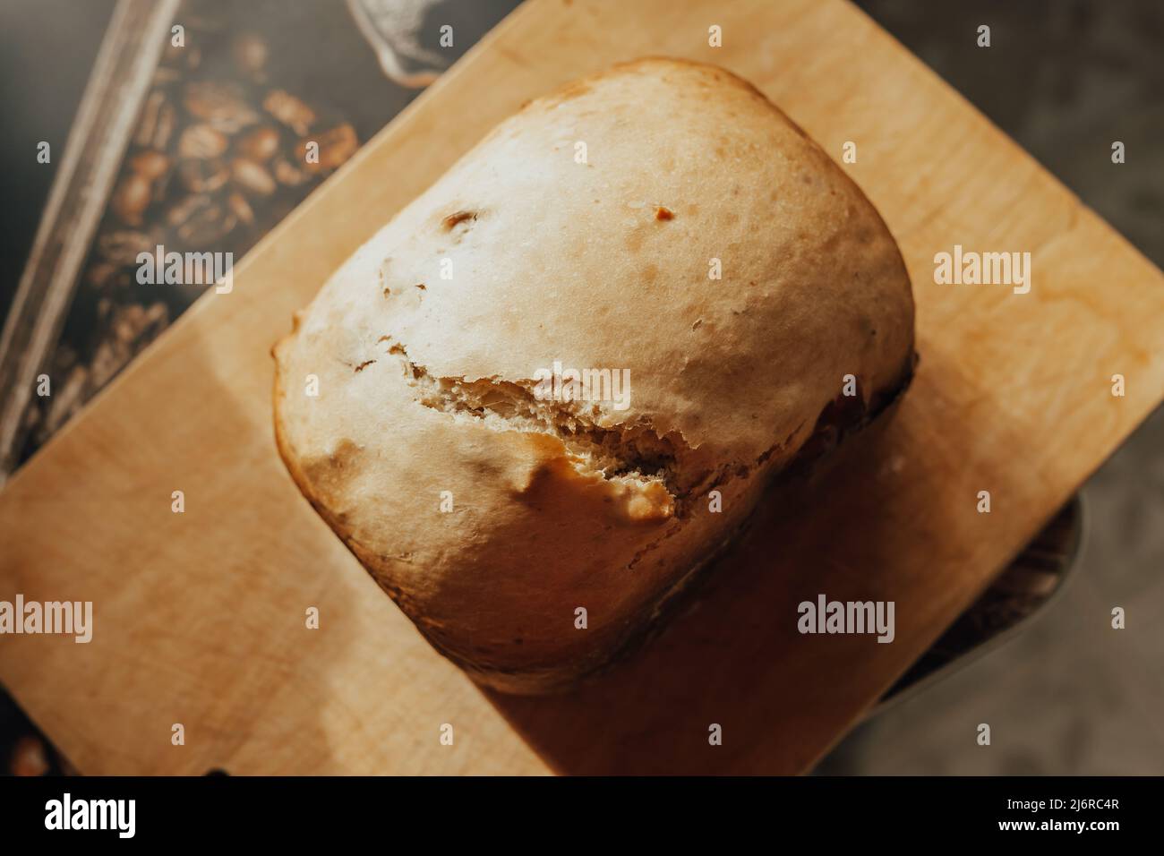 Ein Laib frisches, flauschiges hausgemachtes Brot, das in einer Brotmaschine auf einem Holzbrett gebacken wird. Stockfoto