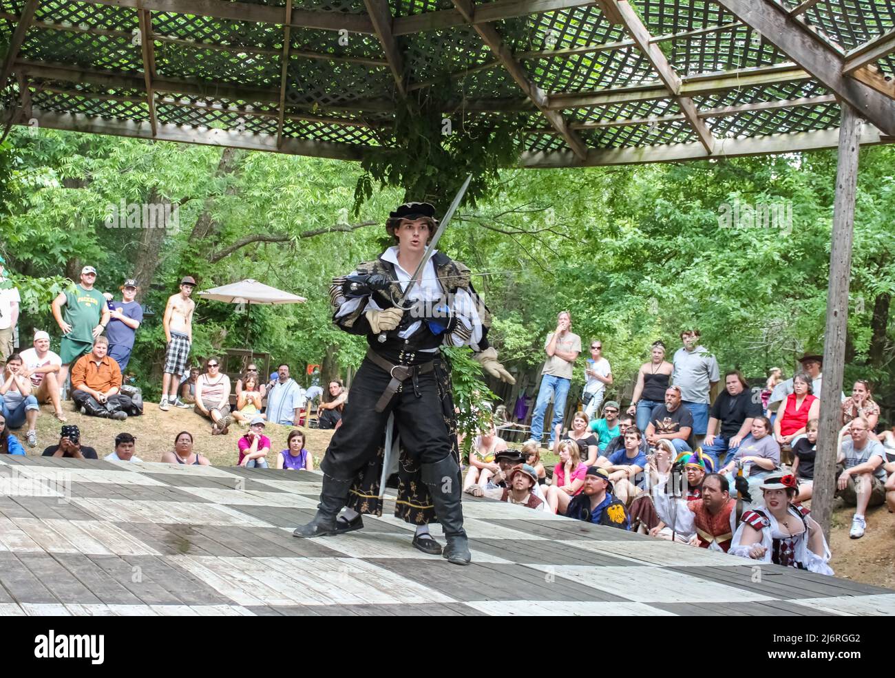 Kämpfer in mittelalterlichem Kostüm sieht erstaunt aus, als eine Kämpferin ihn mit Schwert von hinten ansteckt und die Leute Renassiane Festival Muskogee OK USA May 22 Stockfoto