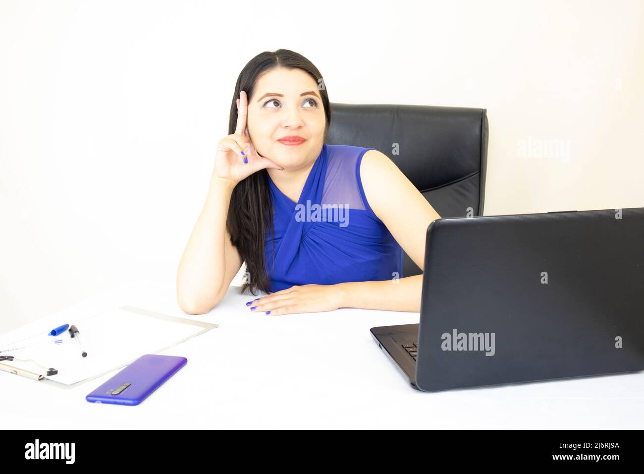 Schöne, elegante Assistentin der Geschäftsführerin, in blauer Bluse, denkt an ihre Zukunft, arbeitet hart am Schreibtisch und Laptop, auf weißem Hintergrund Stockfoto