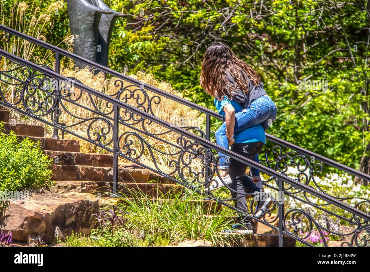 High School Kids goofing herum im Park - Junge klettert Treppe mit langhaarigen Mädchen reiten Piggy Rücken - selektive Fokus und Bewegung verschwimmen Stockfoto