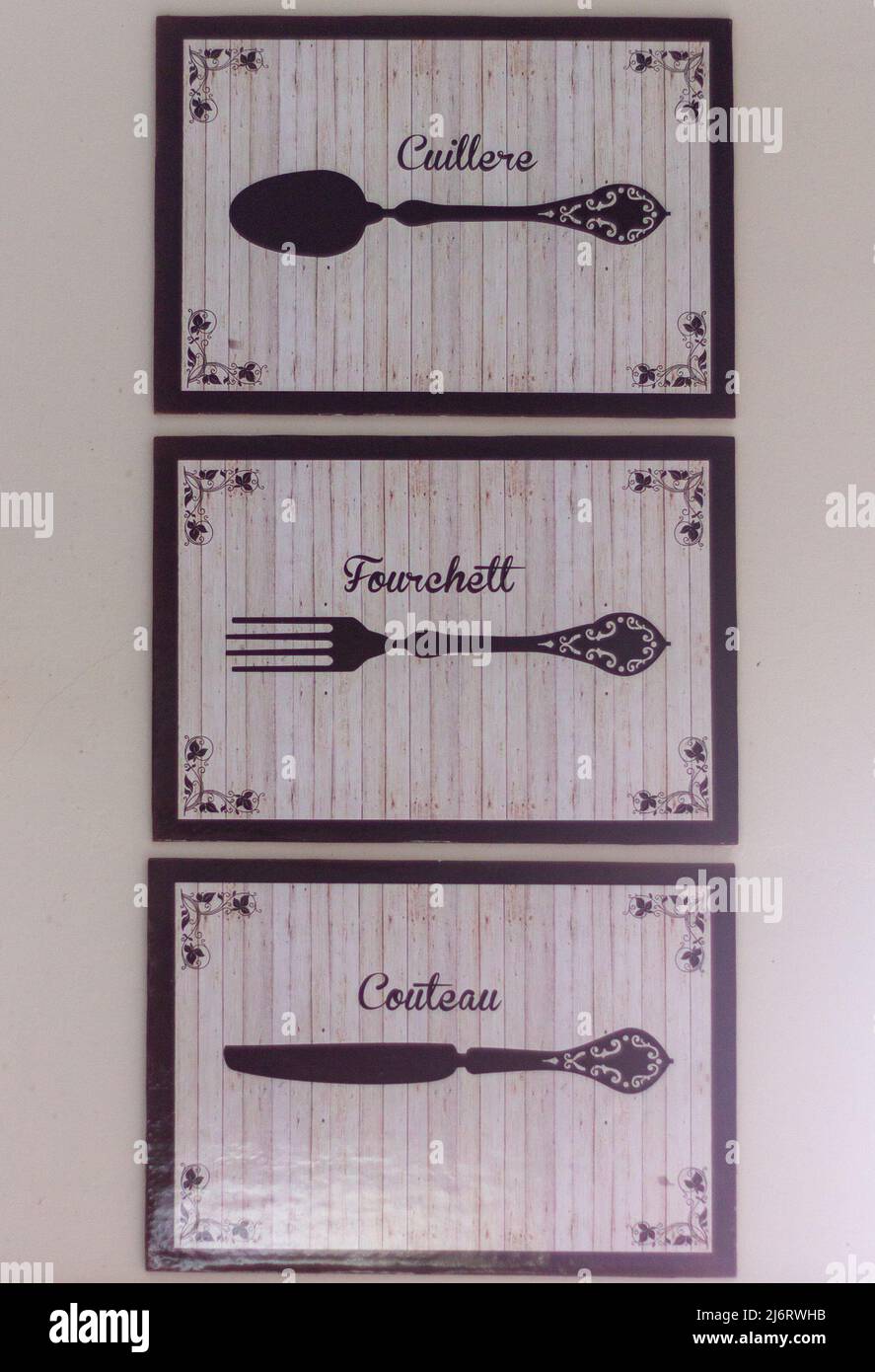 Drei cremefarbene und schwarze Gemälde mit Zeichnungen einer Gabel, eines Messers und eines Löffels, mit Beschreibungen in französischer Sprache an einer Küchenwand Stockfoto