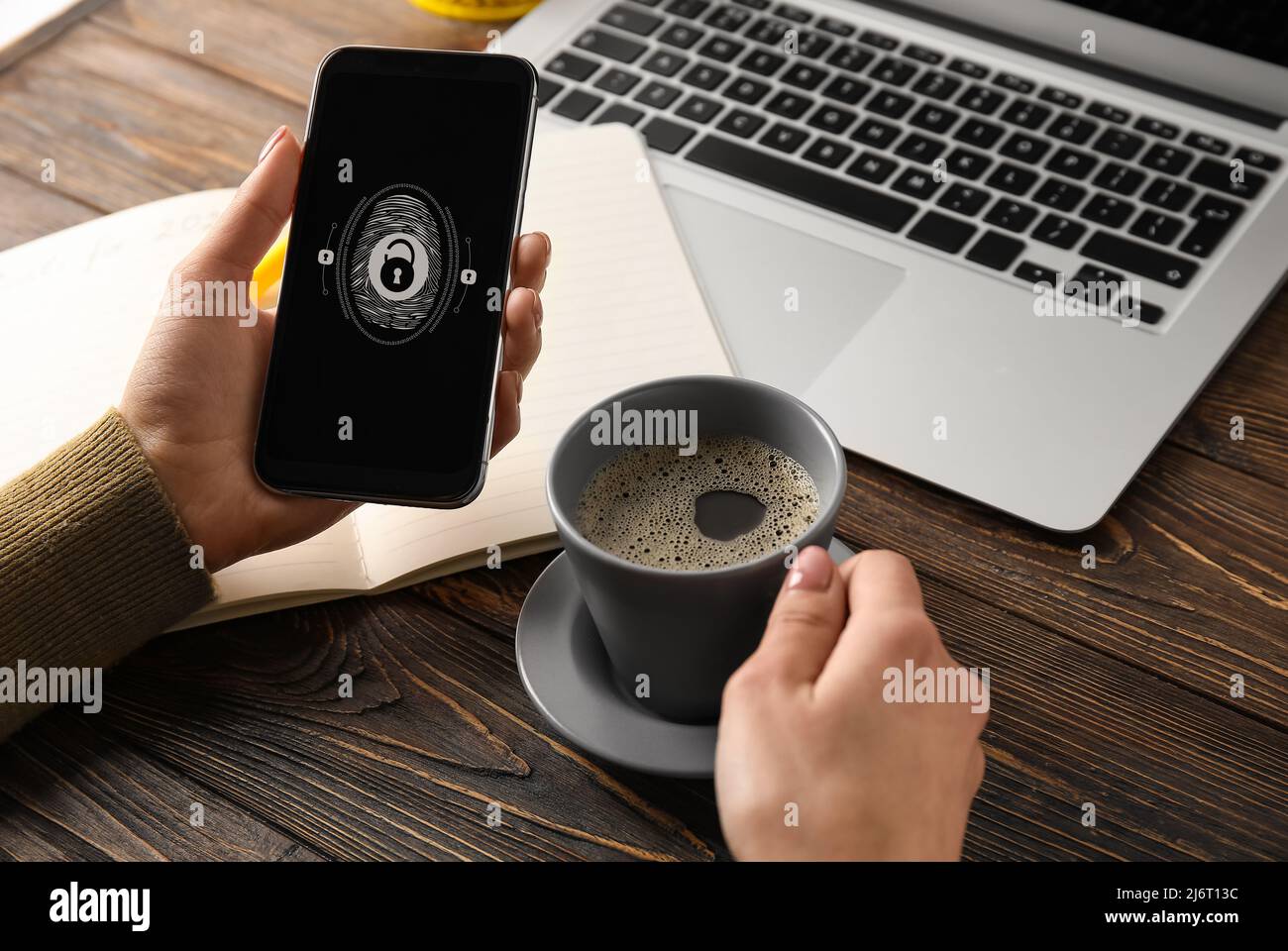 Frau mit Kaffee und Smartphone, die Fingerabdruckscanner verwendet, um sich in Nahaufnahme am Arbeitsplatz in ein persönliches Konto einzuloggen Stockfoto