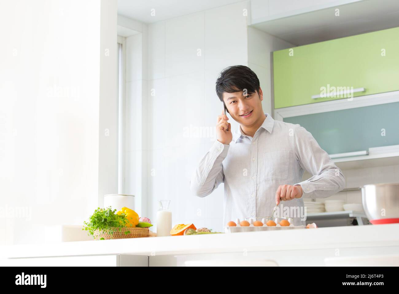 Junger Mann, der in der Familienküche Essen zubereitet, während er am Telefon telefoniert - Stock photo Stockfoto