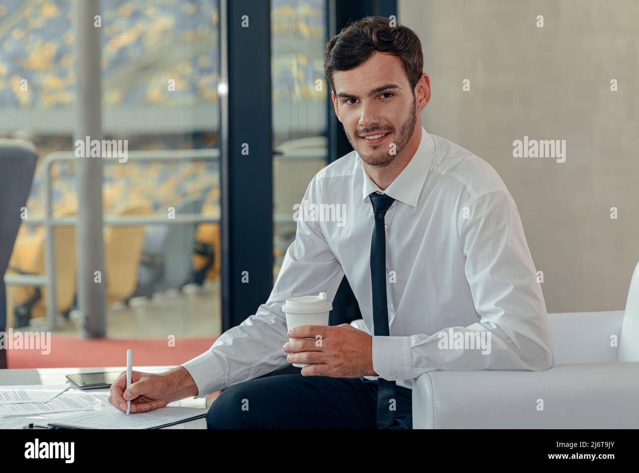 Junger Geschäftsmann sitzt auf einem Sessel im Büro und unterzeichnet Dokumente Stockfoto
