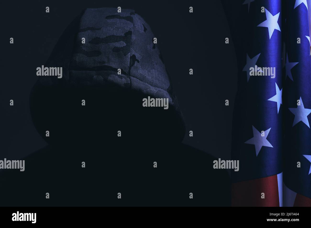 Mann dunklen Hintergrund Kapuze mit verborgenem Gesicht in dunkel, steht nächste Flagge USA America.Hacker Angreifer und Bandit Stockfoto