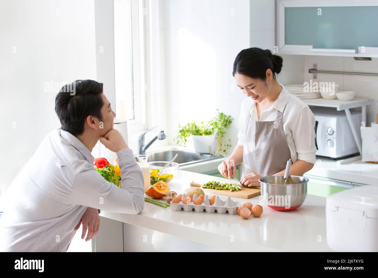 In der Familienküche kocht das junge Paar gerne zusammen. Ehemann blickt liebevoll auf Frau hackt Gemüse - Stock Foto Stockfoto