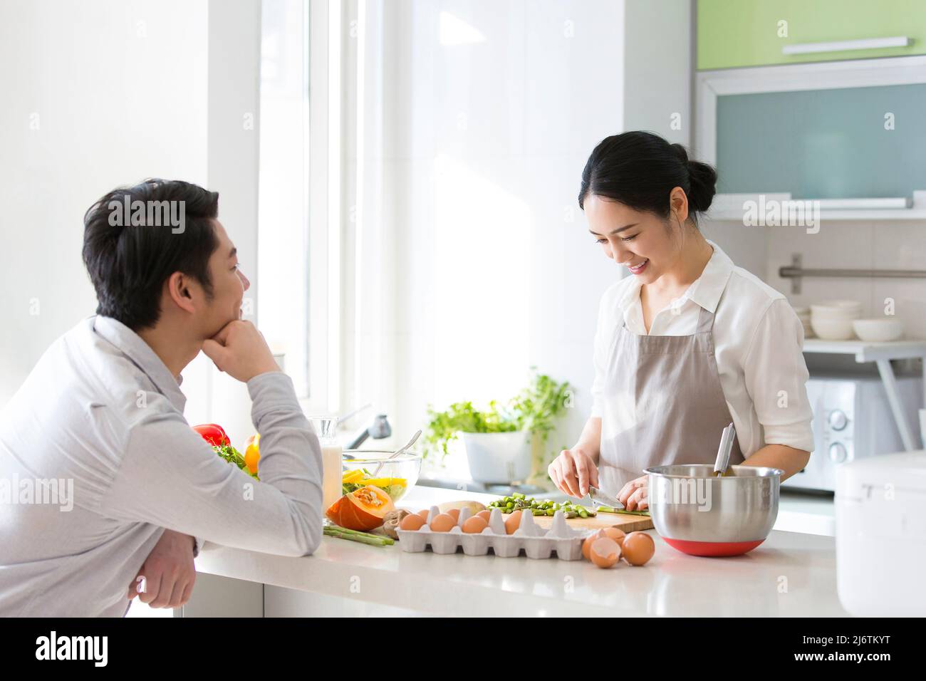 In der Familienküche kochte ein junges Paar zusammen. Ehemann blickte liebevoll auf Frau, die Gemüse hackt - Stock Foto Stockfoto