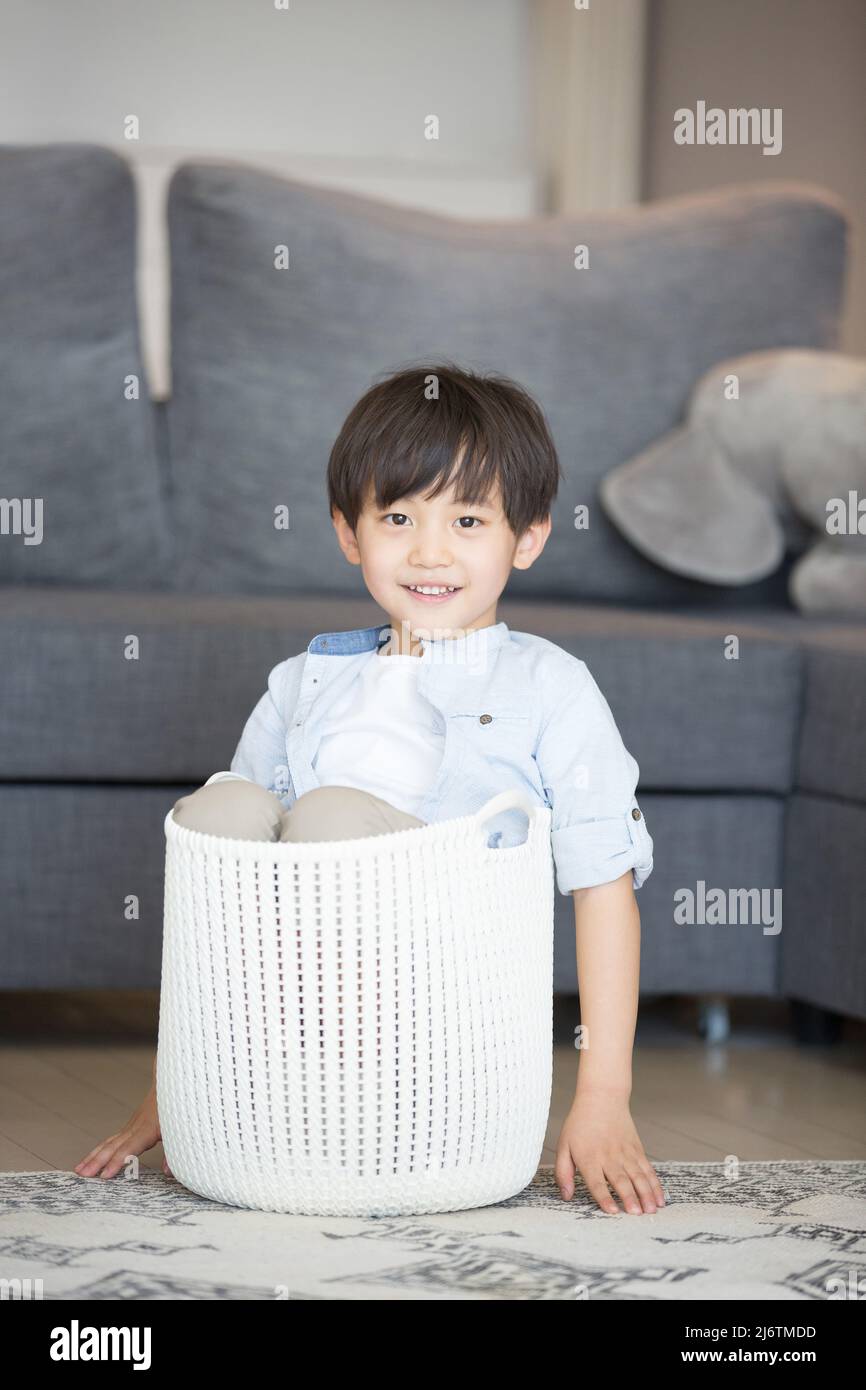 Ein kleiner Junge sitzt in einem Wäschekorb neben dem Wohnzimmer Sofa - Stock Foto Stockfoto