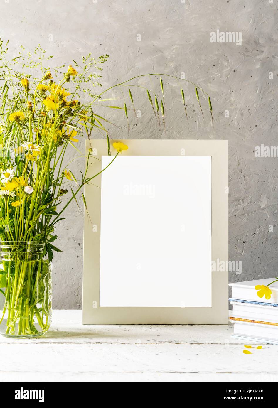 Modellerstellung. Weißer Rahmen auf weißem Holztisch mit grauem Betonhintergrund und wilden Frühlingsblumen Stockfoto