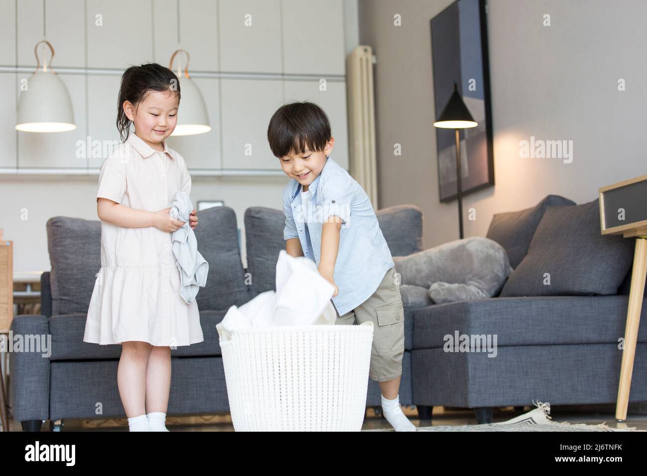 Auf dem Sofa im Wohnzimmer konkurrieren die beiden Geschwister, um die zu waschenden Kleider in den Wäschekorb zu legen - Stock photo Stockfoto