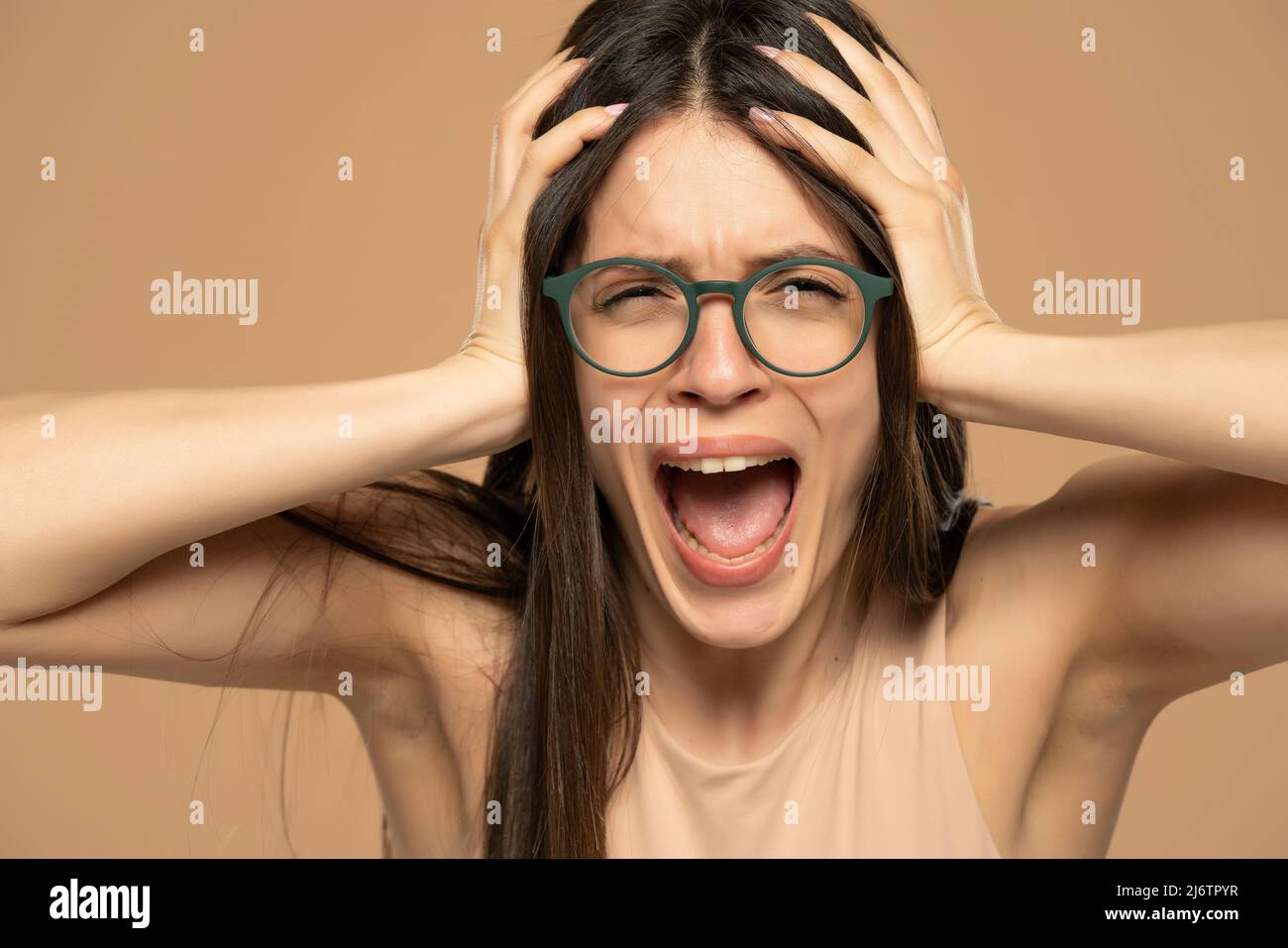 Nahaufnahme Porträt gestresst frustriert Frau mit Brillen Schreien isoliert auf beigem Hintergrund. Negative Gesichtsexpression des menschlichen Gefühls Reaktion A Stockfoto