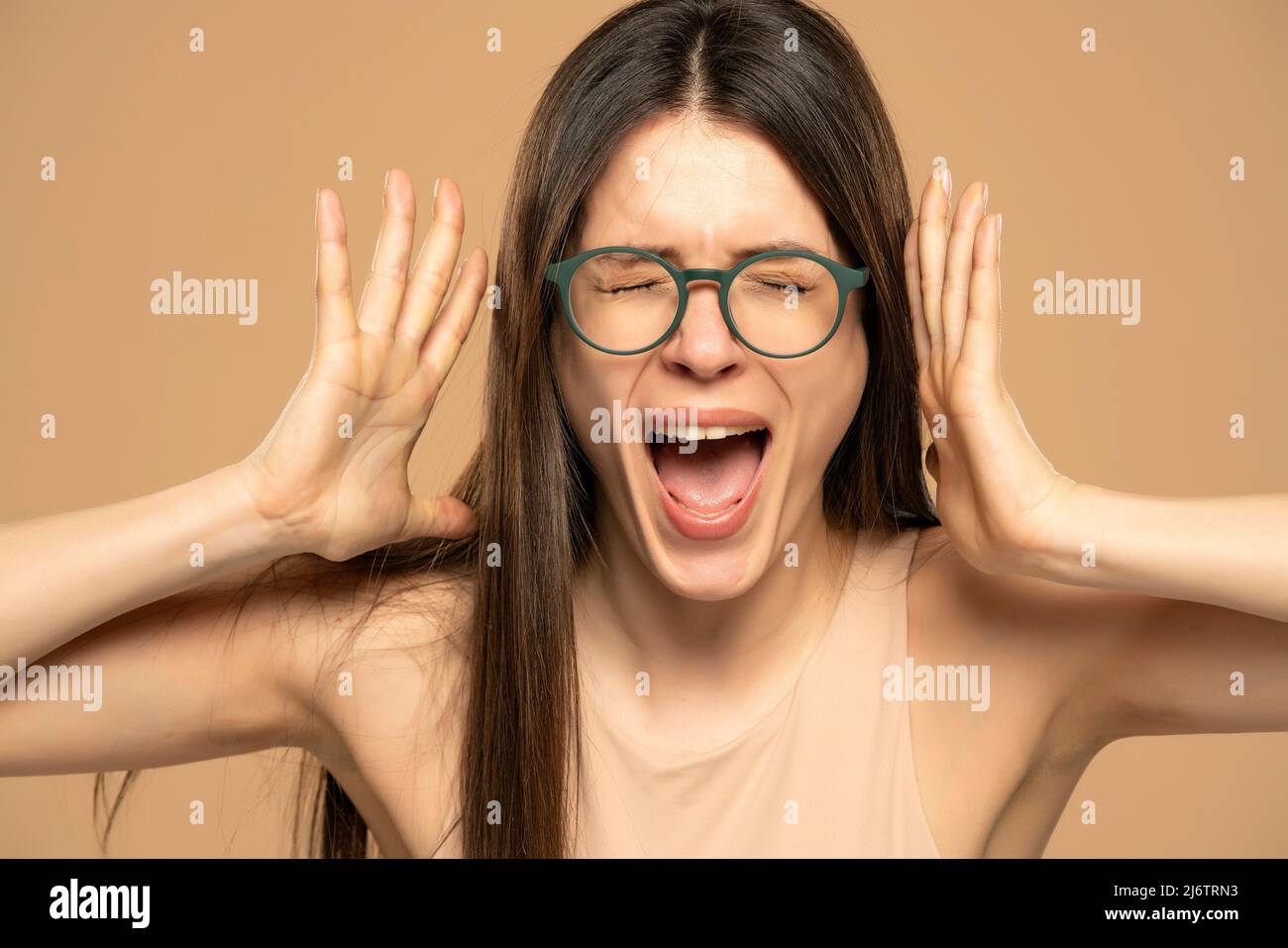 Nahaufnahme Porträt gestresst frustriert Frau mit Brille schreiend mit Temperament Tantrum isoliert auf beigem Hintergrund. Negative menschliche Emotionen Gesichtsbehandlung ex Stockfoto