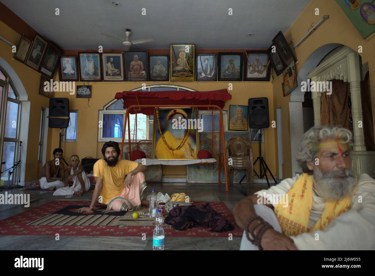 Ein hingebungsvoller Sadhu, ein Hausmeister und Studenten in einem Saal, der mit einem großen gedruckten Foto von Shri Satuwa Baba Maharaj (1913-2012), dem sechsten Satuwa Baba, dem letzten spirituellen Führer beim Shri Satuwa Baba Ashram in Varanasi, Uttar Pradesh, Indien, geschmückt ist. Stockfoto