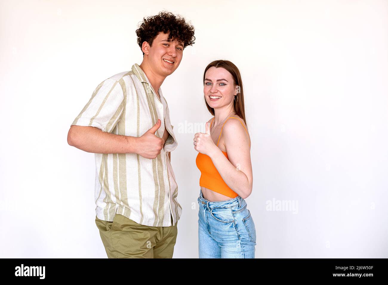 Porträt von jungen fröhlichen Paar posiert auf weißem Hintergrund. Junge, lockig lächelnde Männer und Frauen zeigen Daumen nach oben. Stockfoto