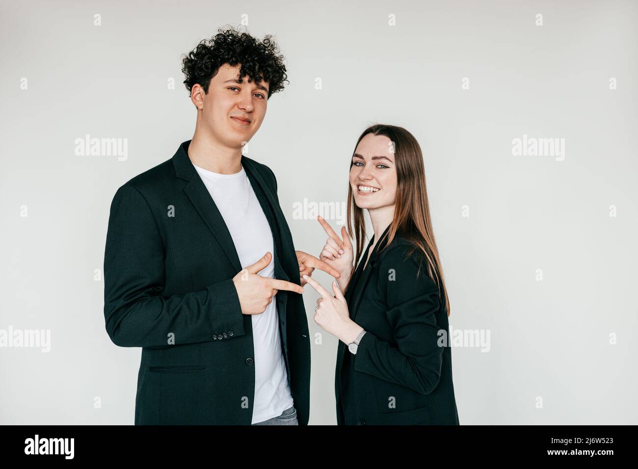 Porträt eines jungen Paares in schwarzer Kleidung. Junger glücklicher Mann, der in der Nähe einer lächelnden Frau steht und auf einander zeigt. Stockfoto