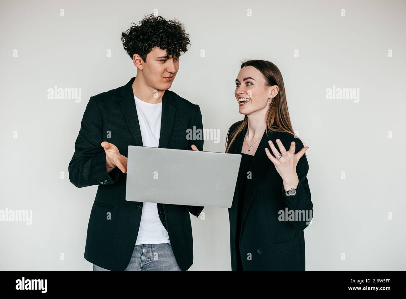 Porträt eines jungen überemotionalen Paares in Schwarz. Junger zufriedener Mann, der überfröhte Frau mit einem Laptop zeigt. Stockfoto
