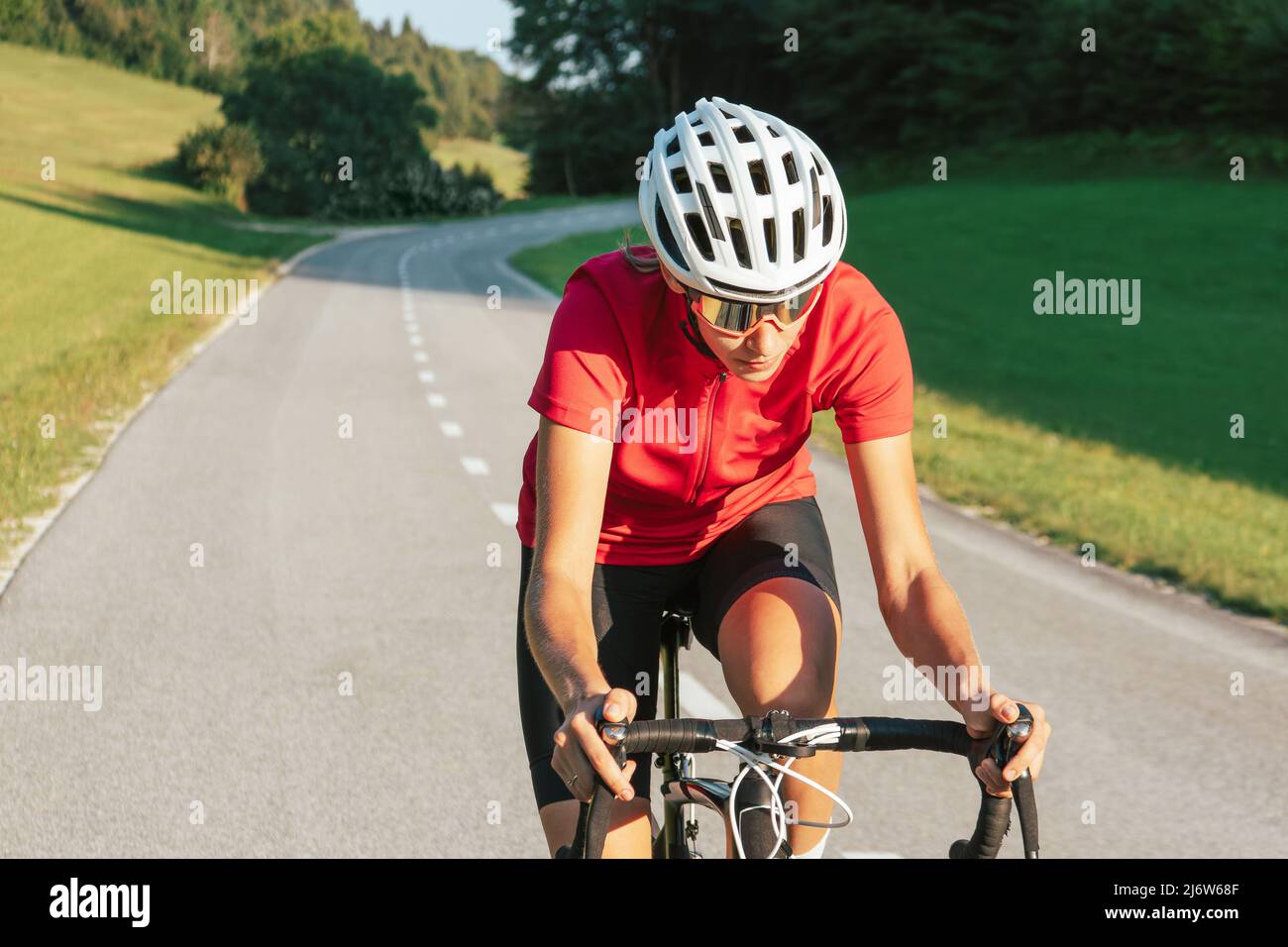 Junge kaukasische Radfahrerin in Sprintposition auf dem Fahrrad während des schnellen Rennradrennens, Vorderansicht. Stockfoto