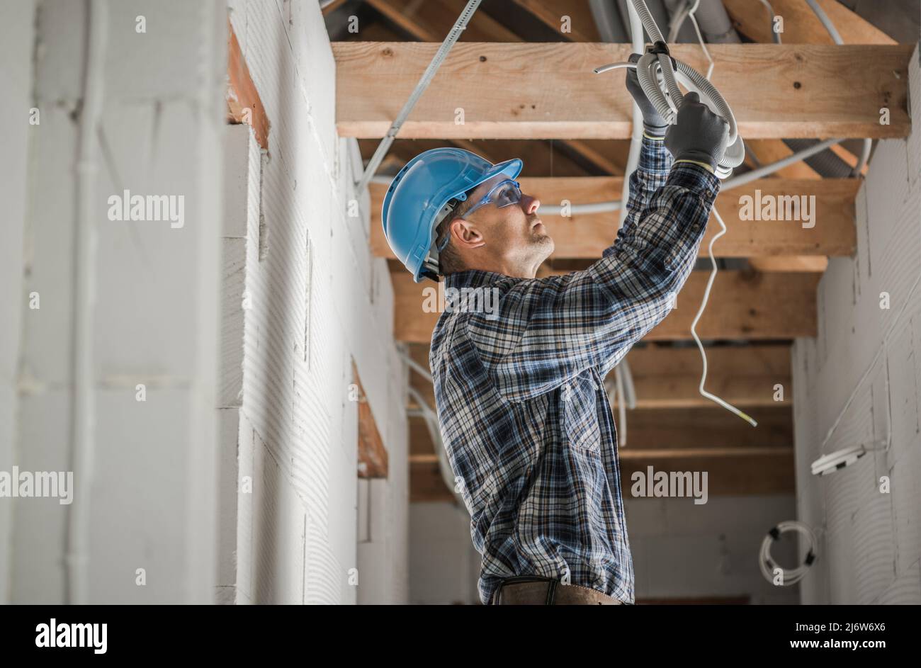 Kaukasische Professional Elektriker in seinem 40s Installation von Decke Lichtpunkt in neu entwickelten Beton Backstein Haus mit Holzbalken Dach Struct Stockfoto