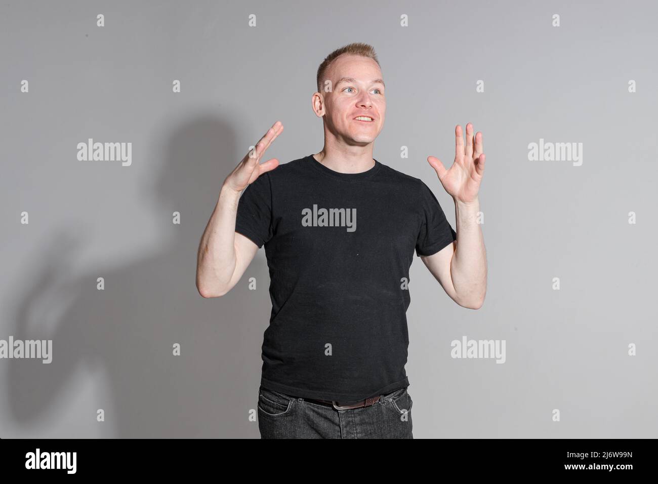 Lebhafter kaukasischer Mann in schwarzem Hemd posiert auf grauem Hintergrund Stockfoto
