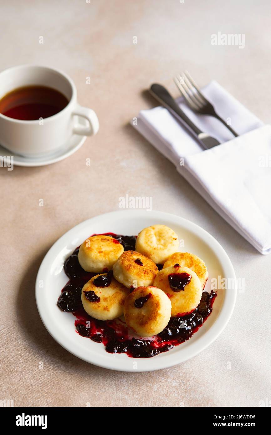Quark-Pfannkuchen, Syrniki, Ricotta-Fritten auf weißem Keramikplatte mit saurer Rahm und Marmelade. Gesundes und leckeres Frühstück am Morgen. Beigefarbener Rücken Stockfoto