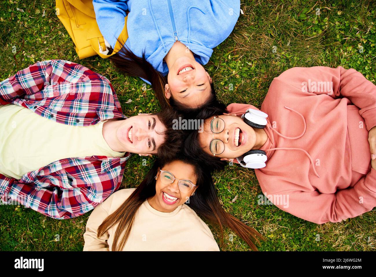 Selbstbewusste multirassische Gruppe von Studenten, die Bücher halten und die Kamera lächeln, die im Kreis auf dem Rasen liegt. Fröhliche junge Menschen, die Spaß haben Stockfoto