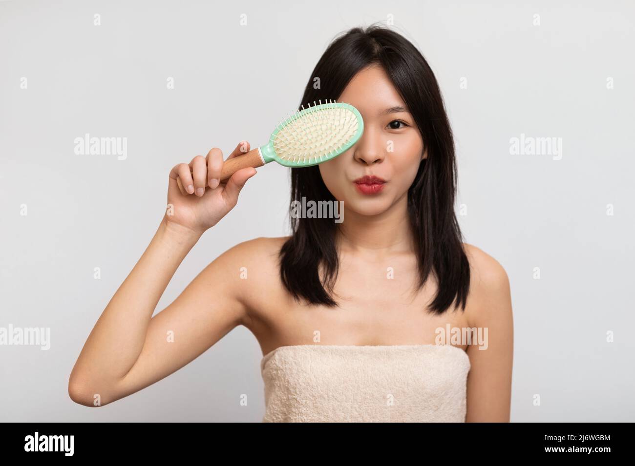 Porträt einer fröhlichen asiatischen Frau, die mit Haarbürste posiert Stockfoto