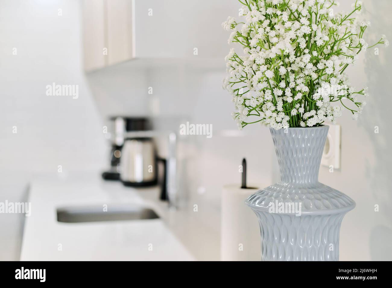 Nahaufnahme von niedlichen kleinen weißen Gypsophila-Blumen in grauer stilvoller Vase auf der Küchentheke, keine Menschen. Moderner Wohnzimmerhintergrund Stockfoto