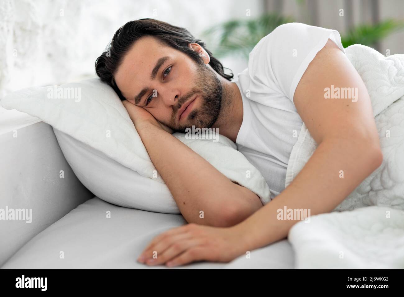 Deprimierter Mann, der allein im Bett lag und sich den Platz der Kopie ansah Stockfoto